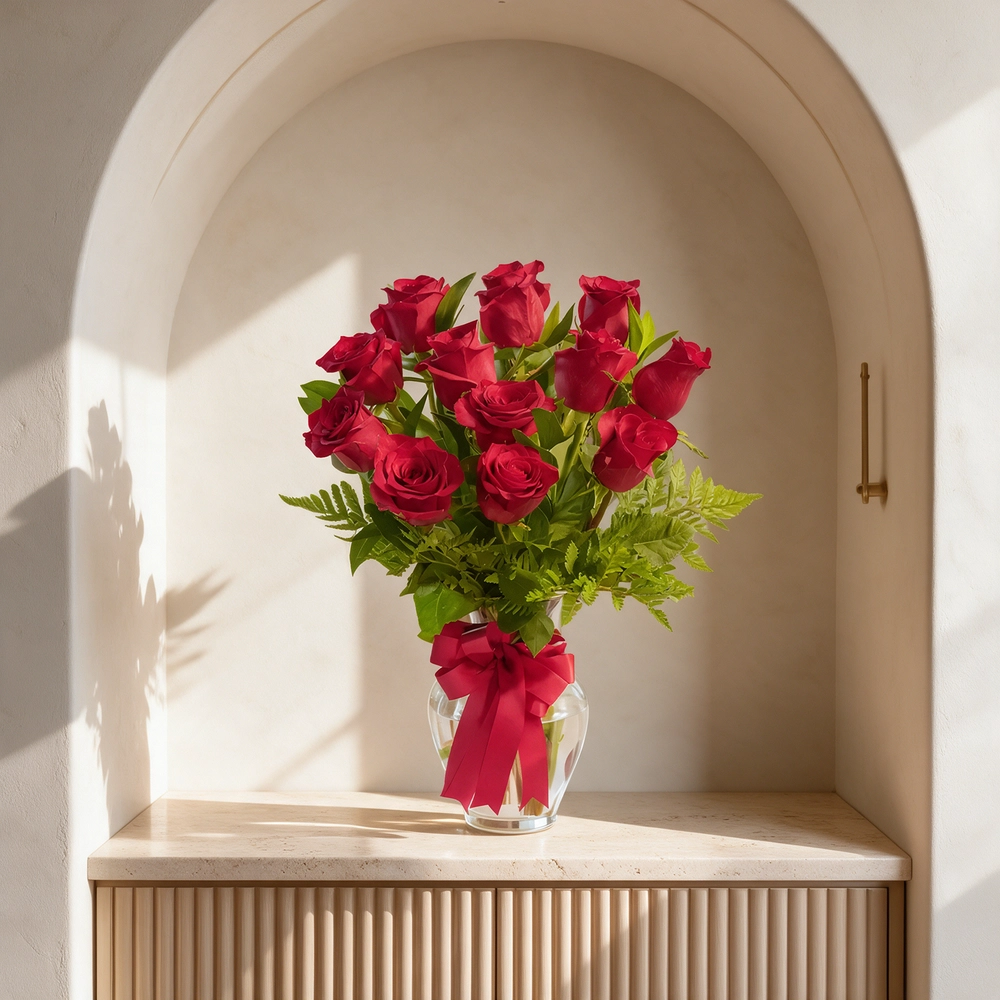 Clear glass vase with 12 red roses, eucalyptus, and green foliage, tied with a red satin ribbon.
