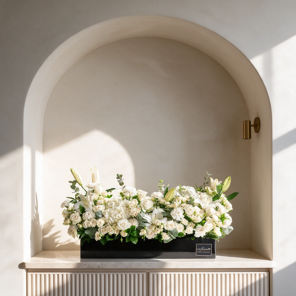 Arrangement of 5 white lilies, 20 white roses, 20 white spray roses, 10 white carnations and 2 white hydrangeas with green fillers in a long black box.